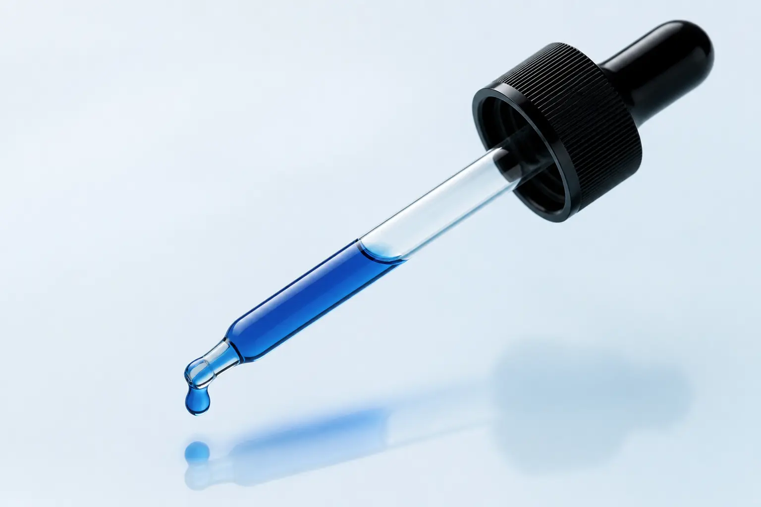 Macro glass pipette filled with blue methylene blue liquid and suspended droplet