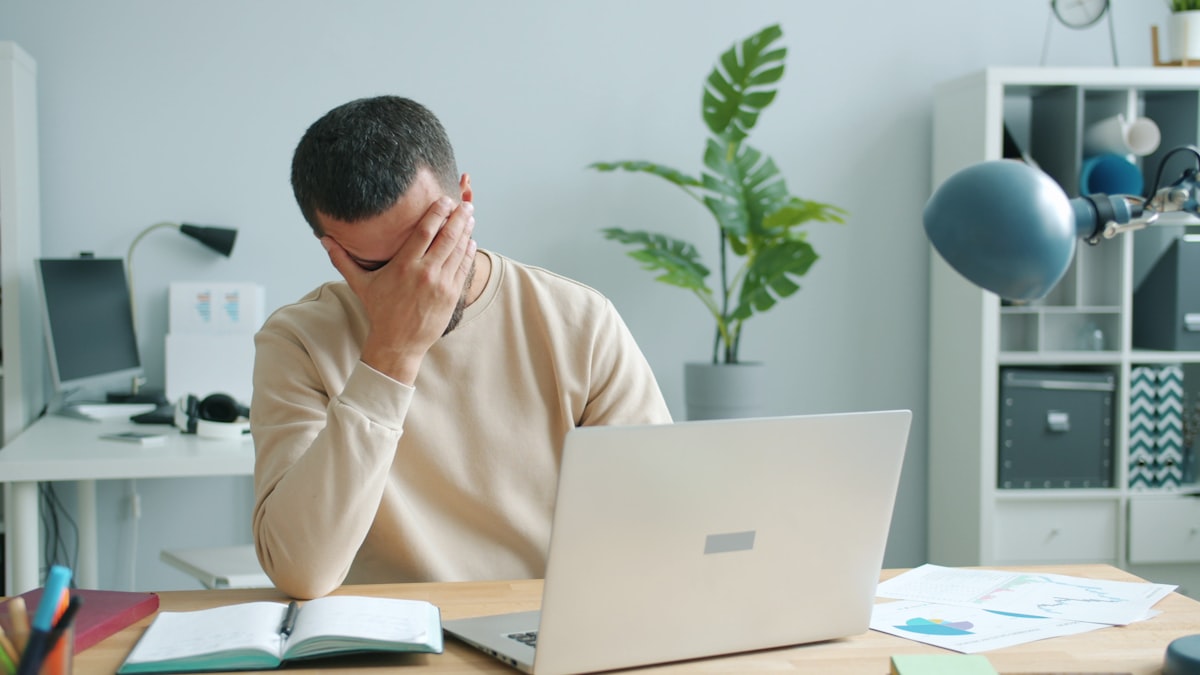 What causes brain fog: a tired man rubbing his face in front of a laptop