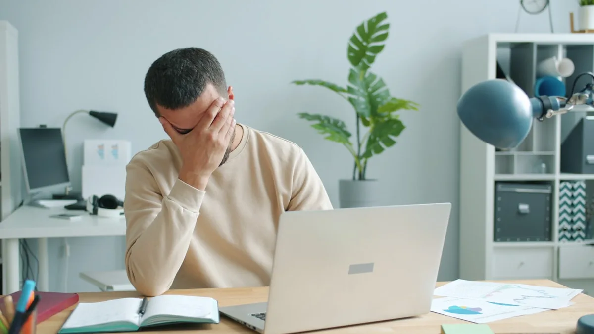 What causes brain fog: a tired man rubbing his face in front of a laptop