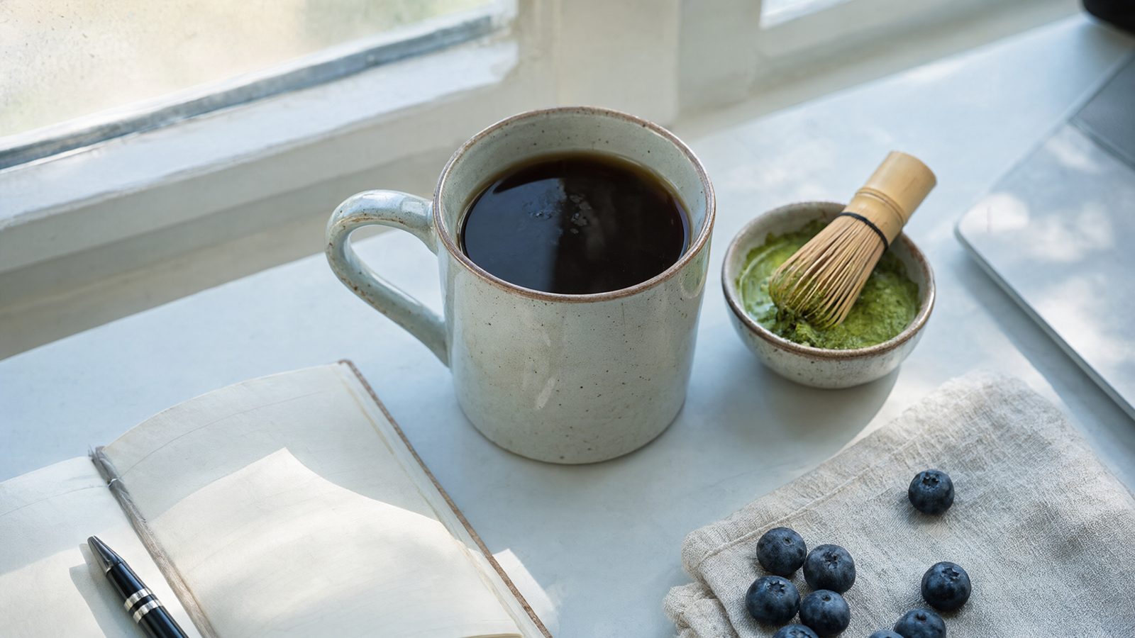 Best caffeine alternatives for focus: a mug of herbal brew, a bowl of matcha and blueberries on a morning desk