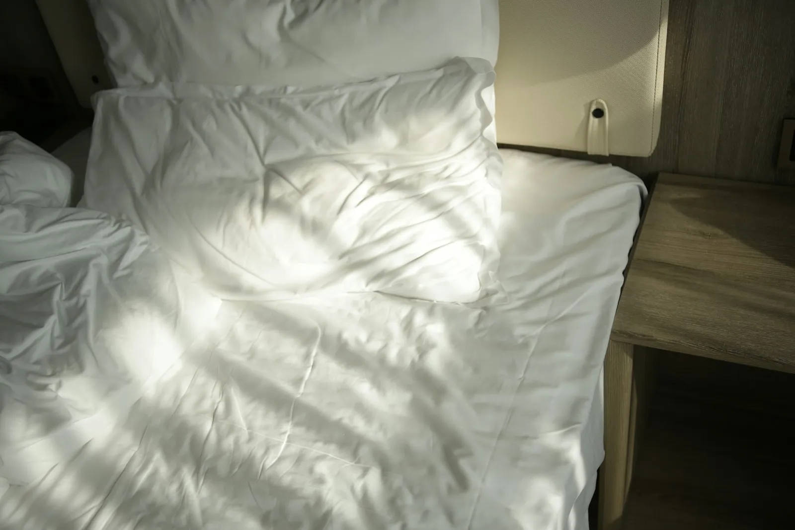 Rumpled white bed in morning sunlight after a short night, a common cause of brain fog from lack of sleep
