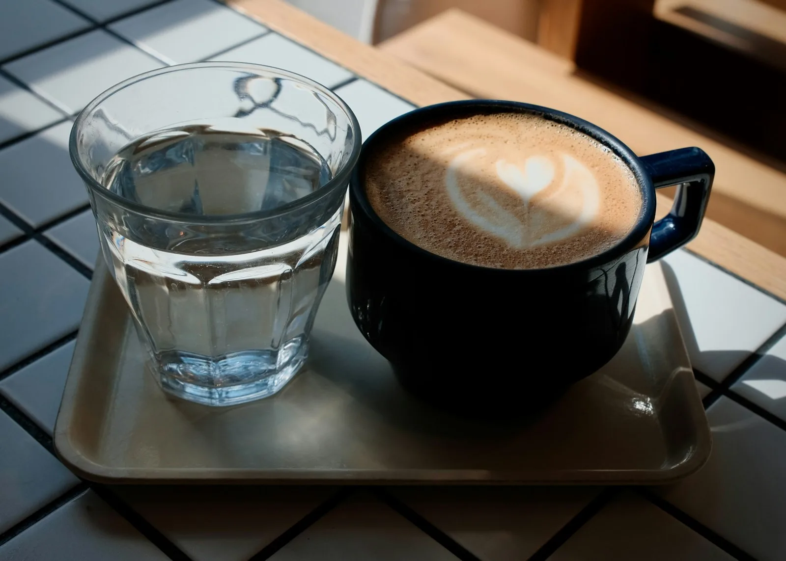 Caffeine tolerance: a latte in a blue mug beside a glass of water on a breakfast tray