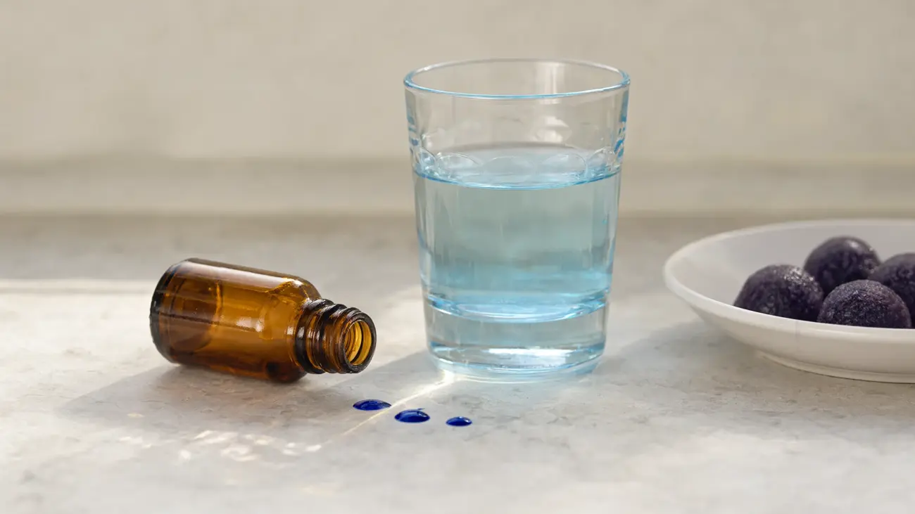 Thinbi methylene blue review: amber dropper bottle, blue drops and a glass of tinted water beside a dish of methylene blue gummies