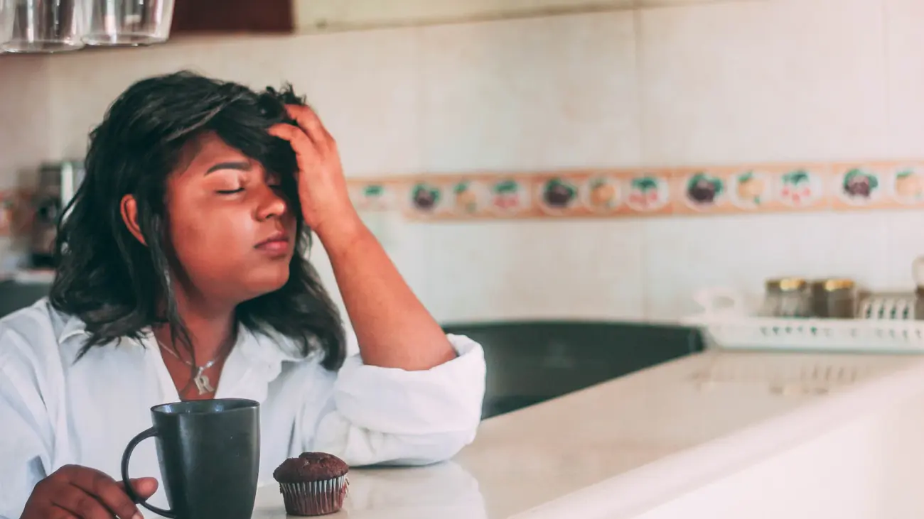 Why am I always tired: woman resting her head on her hand beside a coffee mug in the morning